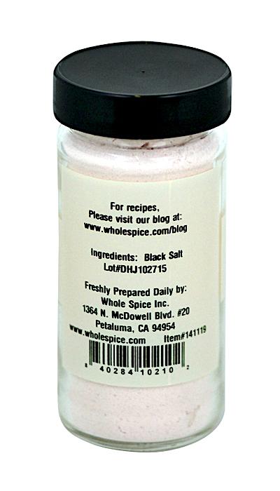 A clear glass jar with a black lid labeled "Black Salt (kala Namak)" from Whole Spice Inc. contains pinkish-black Indian mineral salt, lists black salt as the ingredient, and includes manufacturer details, lot number, and a recipe website.