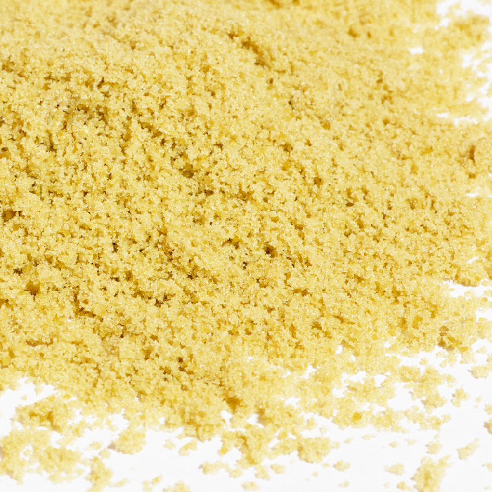 A close-up of fine yellow cornmeal scattered on a white surface, ideal for pairing with Whole Spice Inc. Brown Sugar as a delicious baking sweetener.