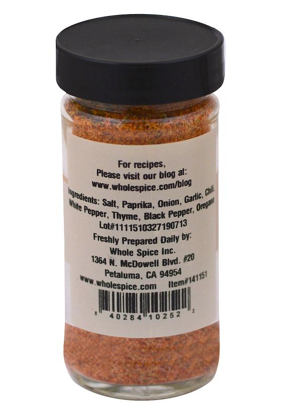 A clear spice jar with a black lid labeled "Cajun Seasoning" by Whole Spice Inc., listing ingredients such as salt, paprika, and chili. The Louisiana-style reddish-orange blend label features their website, address, and a barcode.
