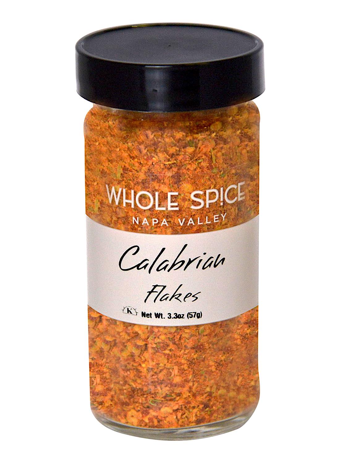 A glass jar labeled Whole Spice Inc. Calabrian Peperoncino Chili Flakes holds orange-red Italian hot peppers, has a black lid, and a net weight of 3.3 oz (57g).