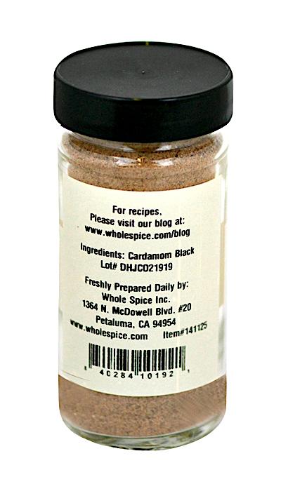 A clear spice jar with a black lid holds Black Cardamom Powder from Whole Spice Inc. The label lists “Cardamom Black” as the ingredient, plus the company address, website, and a barcode—essential for garam masala blends.