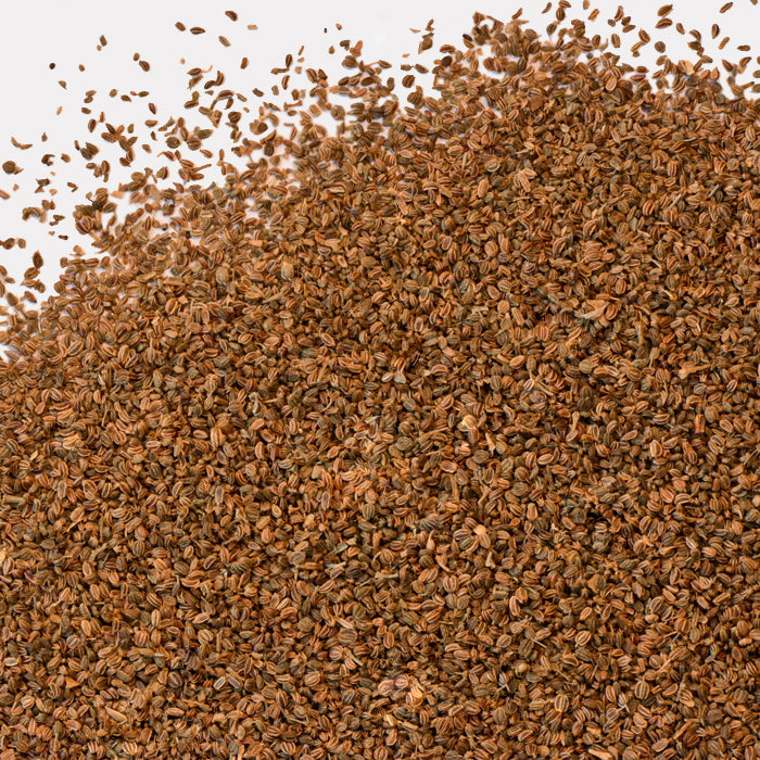 A generous pile of brown, oval-shaped Celery Seeds by Whole Spice Inc. scattered on a white surface—ideal for bringing bold flavor to Mediterranean dishes.