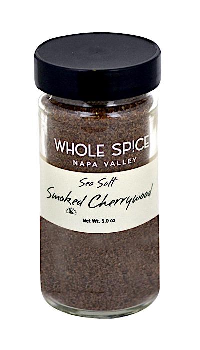 A glass jar with a black lid labeled Whole Spice Inc. Cherrywood Smoked Sea Salt, containing dark brown smoked sea salt for rich, wood-fired flavor. Net weight: 5.0 oz.
