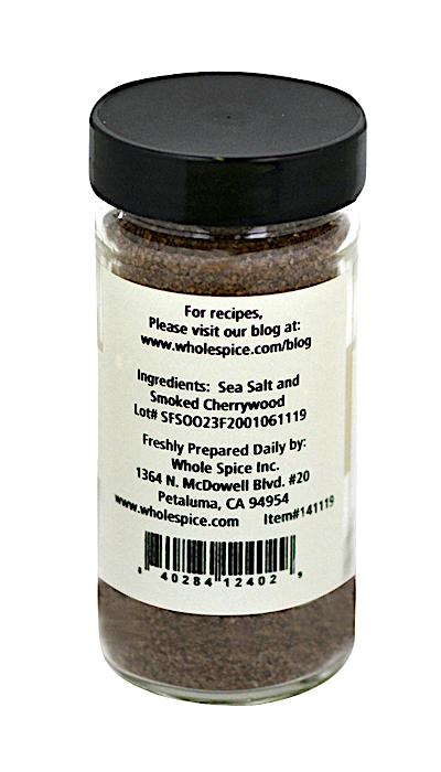 A clear glass jar with a black lid displays Whole Spice Inc.'s white label featuring Cherrywood Smoked Sea Salt ingredients, wood-fired flavor notes, company details, and a barcode.