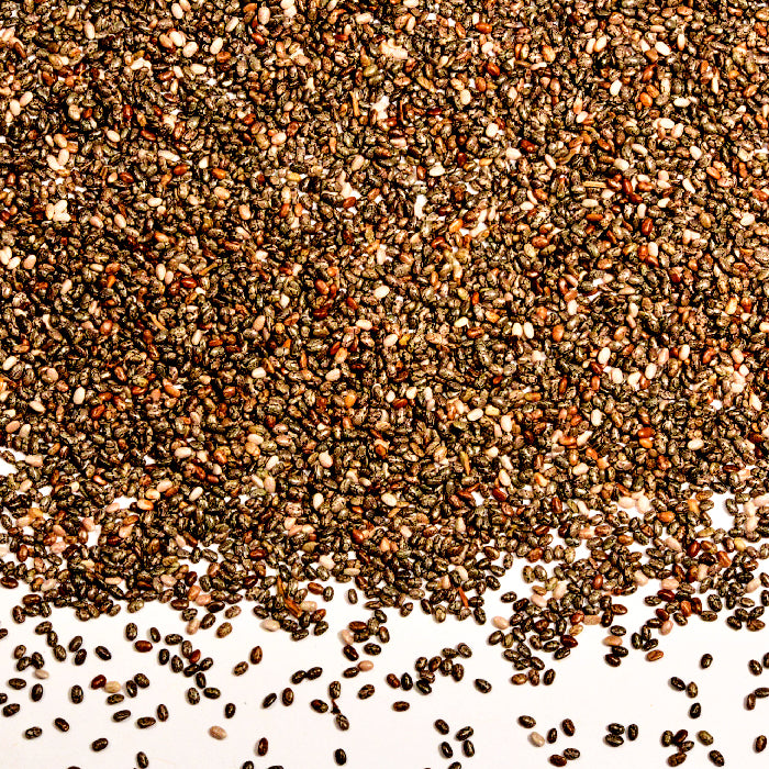 Whole Spice Inc. Chia Seeds, rich in omega-3 fatty acids, are scattered across a white surface, with some seeds loosely spread at the bottom of the image.