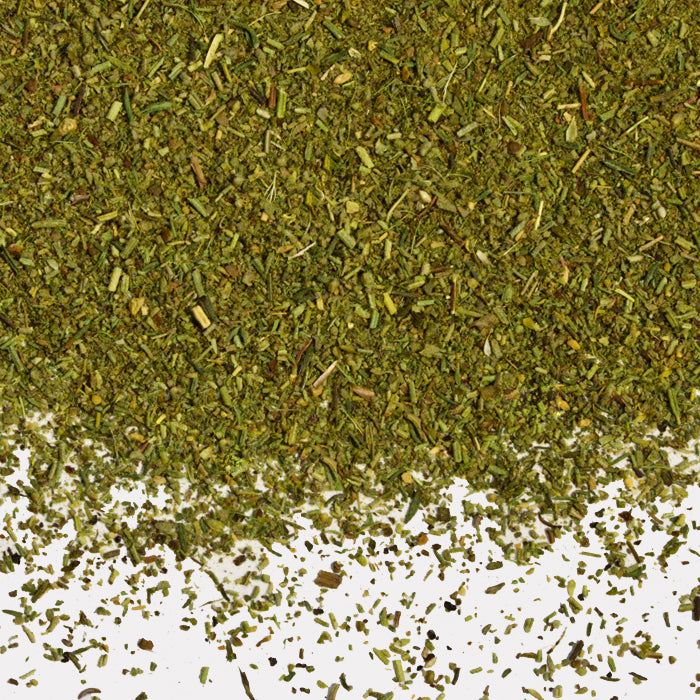 A close-up of Whole Spice Inc. Chicken Stuffing Seasoning, a finely chopped dried green herb blend, is scattered across the upper part of a white surface with small bits dispersed below.