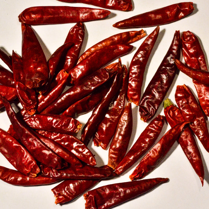 A scattered pile of Whole Spice Inc. Cayenne Chili Whole on a white background highlights their glossy, wrinkled skins and vibrant color—ideal for adding bold chili spice to any recipe.
