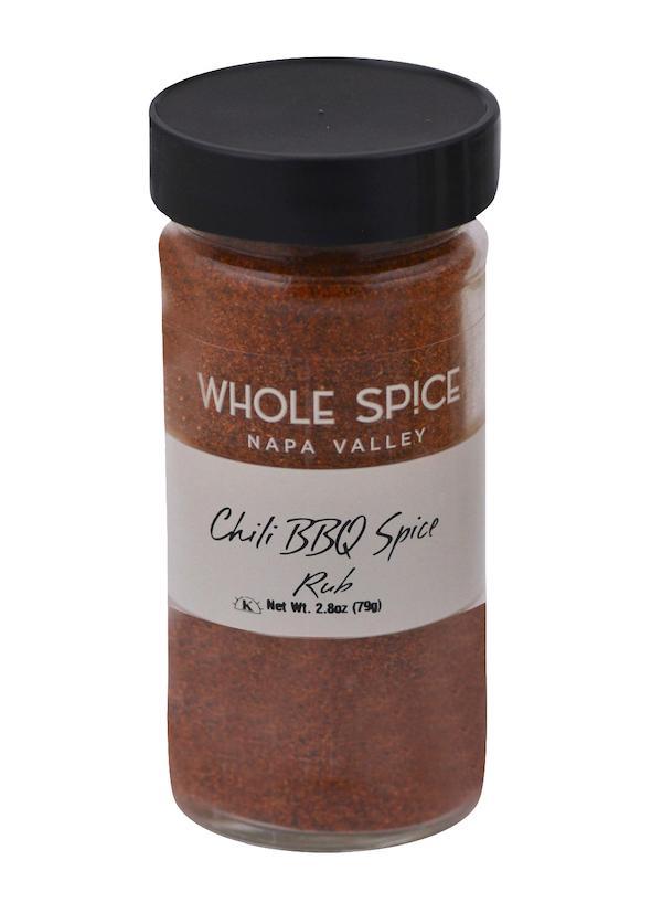 A clear spice jar labeled Chili BBQ Spice Rub by Whole Spice Inc. with a black lid holds a reddish-brown, spicy meat rub blend. Net weight: 2.8 oz (79g).
