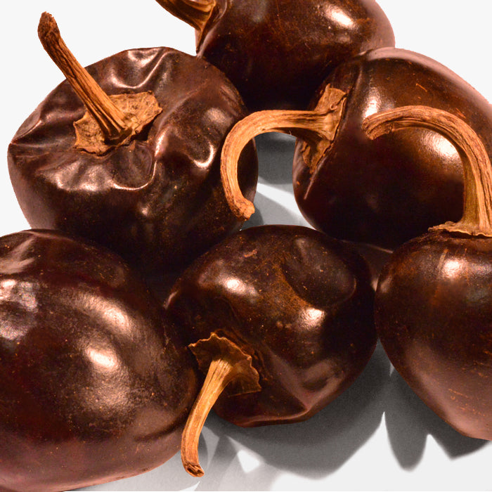 A close-up of Whole Spice Inc. Cascabel Chili Whole—dried, dark brown chilies with wrinkled skins and twisted stems—showcasing their signature rattle and smoky flavor, arranged on a light surface.