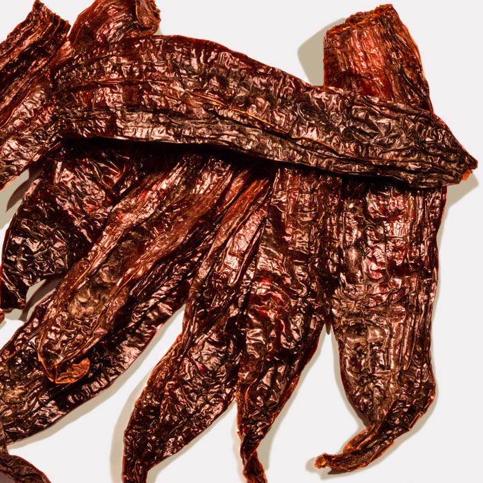 Several dried, wrinkled Aji Amarillo Chili Whole peppers from Whole Spice Inc. are stacked on a light surface, displaying their textured, glossy skin and elongated shape—ideal for adding bold flavor to Peruvian dishes.