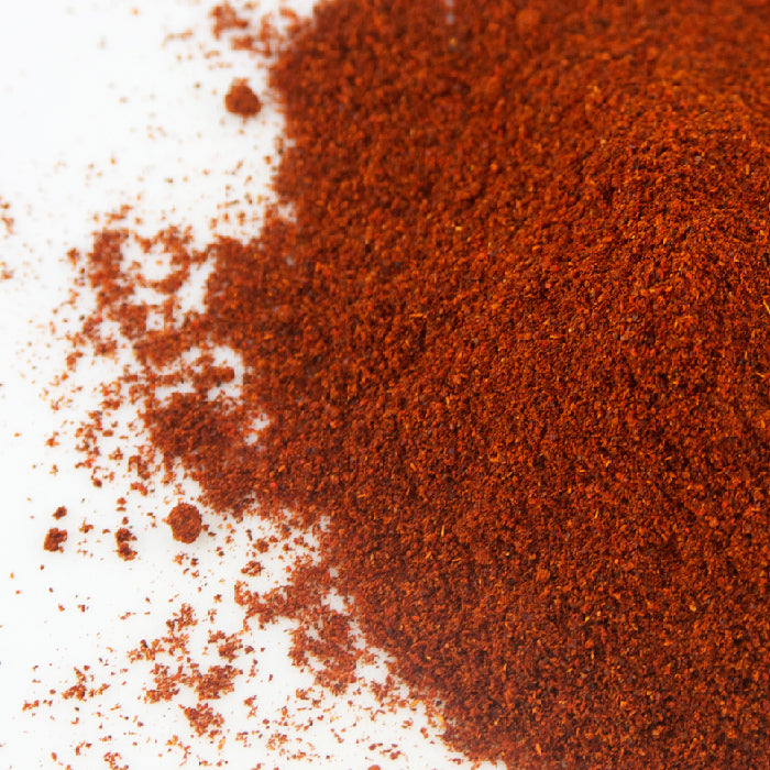 A close-up of Guajillo Chili Powder by Whole Spice Inc., a finely ground red-brown spice scattered on white—a key ingredient in authentic mole sauce.