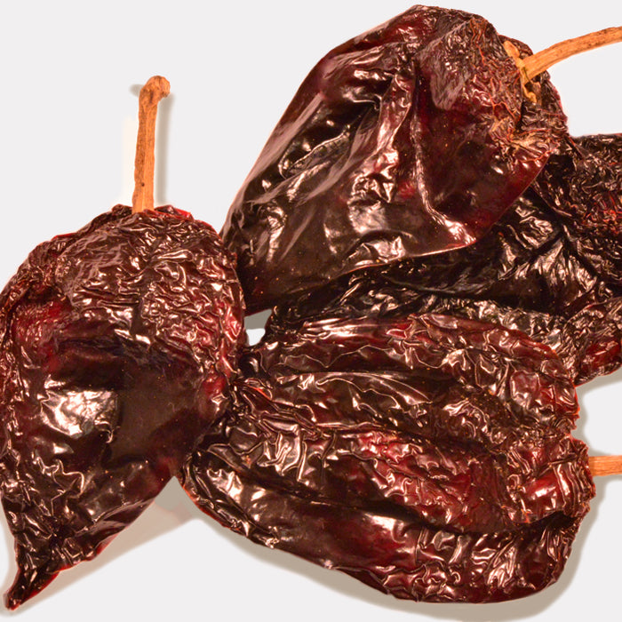 Three Whole Spice Inc. Ancho Chili Whole peppers with wrinkled, glossy reddish-brown skin and attached stems are arranged on a light background—ideal for adding rich flavor to Mexican dishes.