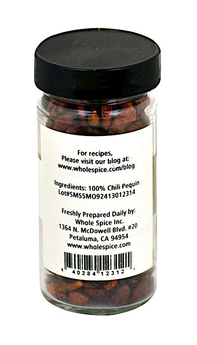 A clear jar of Pequin Chili Whole by Whole Spice Inc. features a white label stating 100% Pequin chili, known for high heat. The label lists recipes website, lot number, and company contact info from Petaluma, CA.