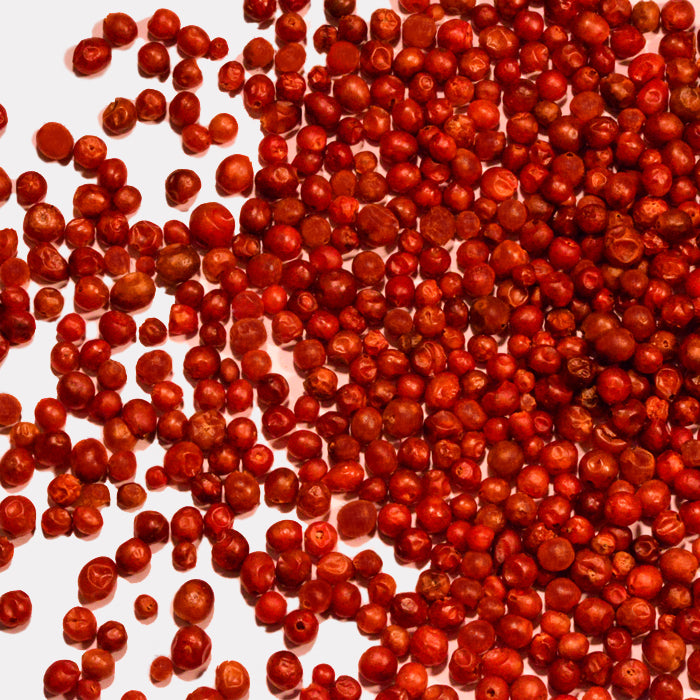 A scattered pile of Whole Spice Inc. Tepin Chili Whole peppers on a white background, with some of these hot peppers loosely spread around the main cluster.