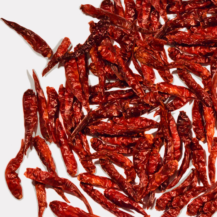 Whole Spice Inc. Thai Chili Whole—dried red chili peppers scattered on a white background—are perfect for adding heat to Thai Basil Curry or spicy peanut sauces.