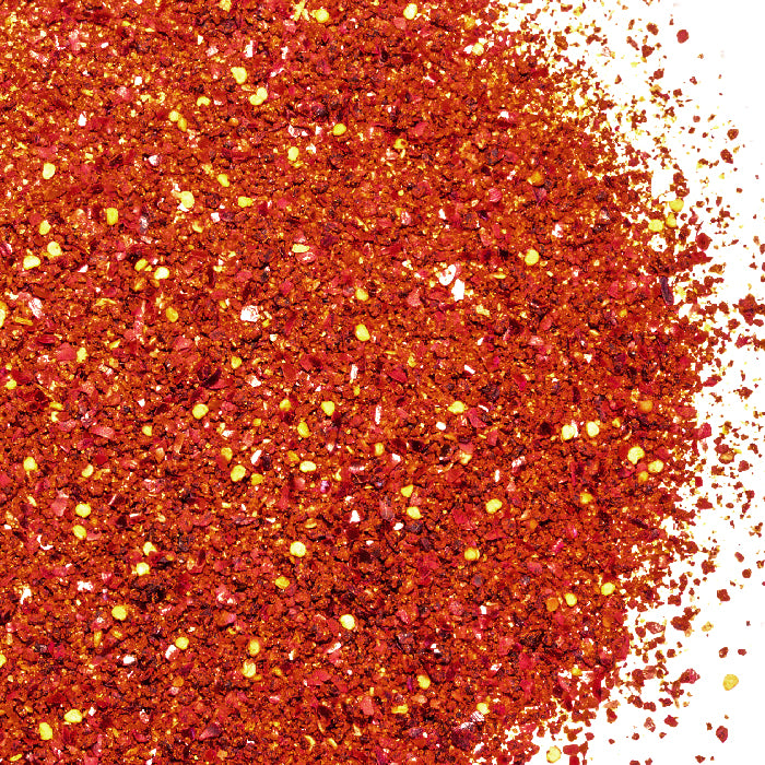 A vibrant pile of red and yellow speckled rocks evokes the look of Whole Spice Inc.'s Chili Lime Salt scattered across a colorful surface.
