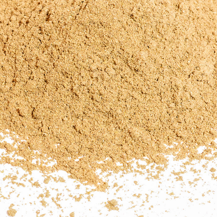 A close-up of Chinese Five Spice by Whole Spice Inc., showing light brown powder scattered on a white surface.