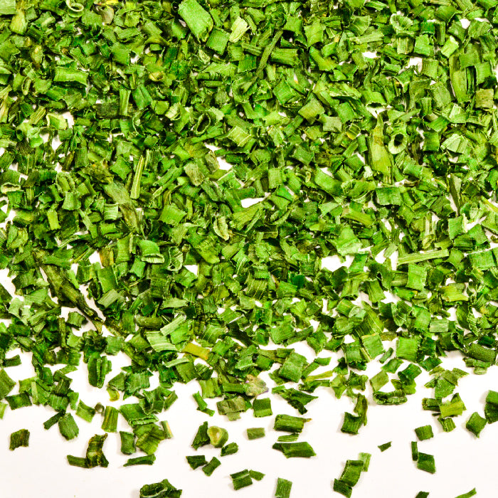 A close-up of Whole Spice Inc. Chives, a dried herb from the onion family, with small green pieces uniformly chopped and scattered on a white background for a vibrant texture.