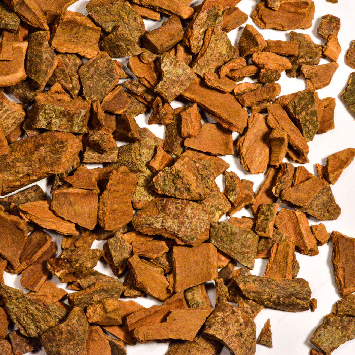 Close-up of Whole Spice Inc.’s Cinnamon Chips Saigon, aromatic brownish fragments with rough, jagged edges scattered on a white background. The bark chips vary in size and texture, resembling natural cinnamon bark.