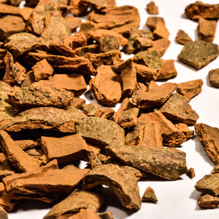 Close-up of scattered Cinnamon Chips Cassia by Whole Spice Inc. on a white surface, showcasing rough textures and rich brown hues—emphasizing this premium spice’s natural form.
