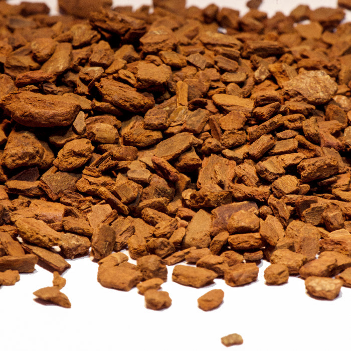 A close-up of Cinnamon Chips Organic by Whole Spice Inc. shows small, irregular pieces scattered on a white surface, resembling traditional Chinese medicine ingredients.