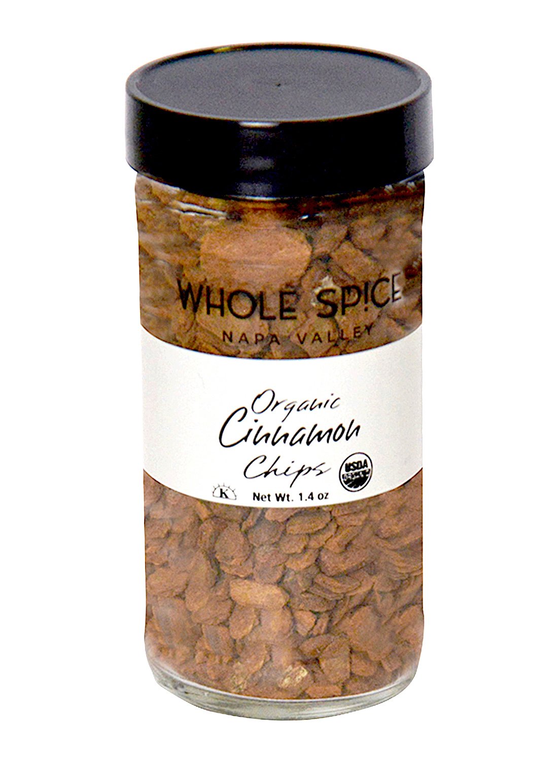 A glass jar with a black lid labeled "Cinnamon Chips Organic" by Whole Spice Inc. contains fragrant brown organic cinnamon chips, prized in traditional Chinese medicine, and features the USDA organic seal.
