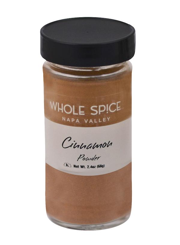A glass jar of Whole Spice Inc. Cinnamon Powder with a black lid and a white label showing the product name and net weight of 2.4 oz (68g).