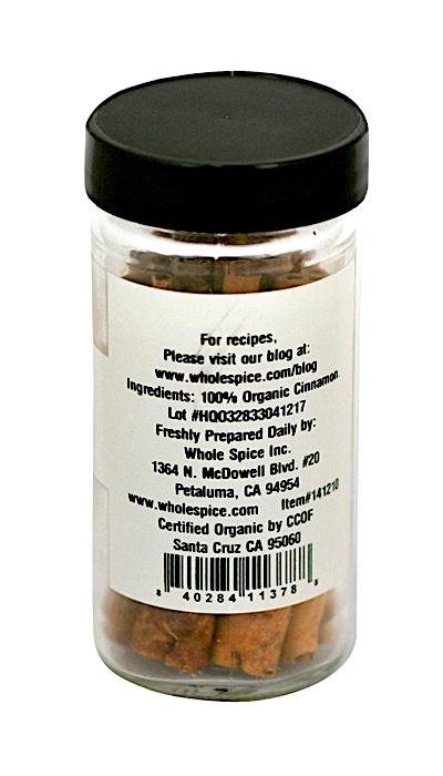 A clear spice jar with a black lid contains Whole Spice Inc. Cinnamon Sticks Organic. The label lists 100% organic cinnamon, certification and company details, its use in traditional Chinese medicine, and displays a barcode at the bottom.