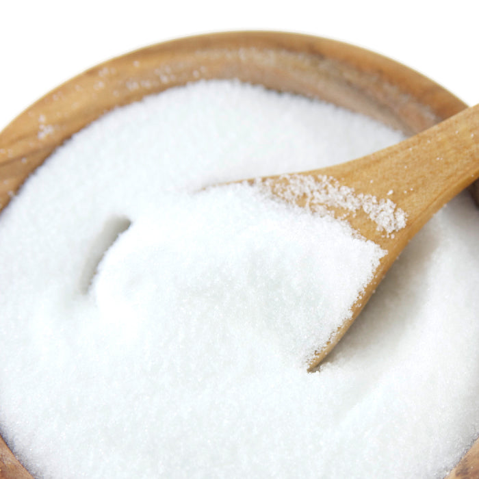 A wooden spoon scoops white citric acid from a wooden bowl—Whole Spice Inc. Citric Acid is ideal for sausage making or adding a tangy flavor to your favorite recipes.