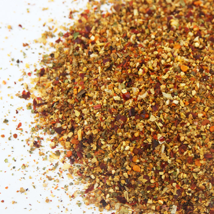 A close-up of Whole Spice Inc.'s colorful Citrus Peel Rub, a vibrant blend of dried spices and citrus peel, scattered on white—perfect for adding zesty flavor to seafood or grilled dishes.