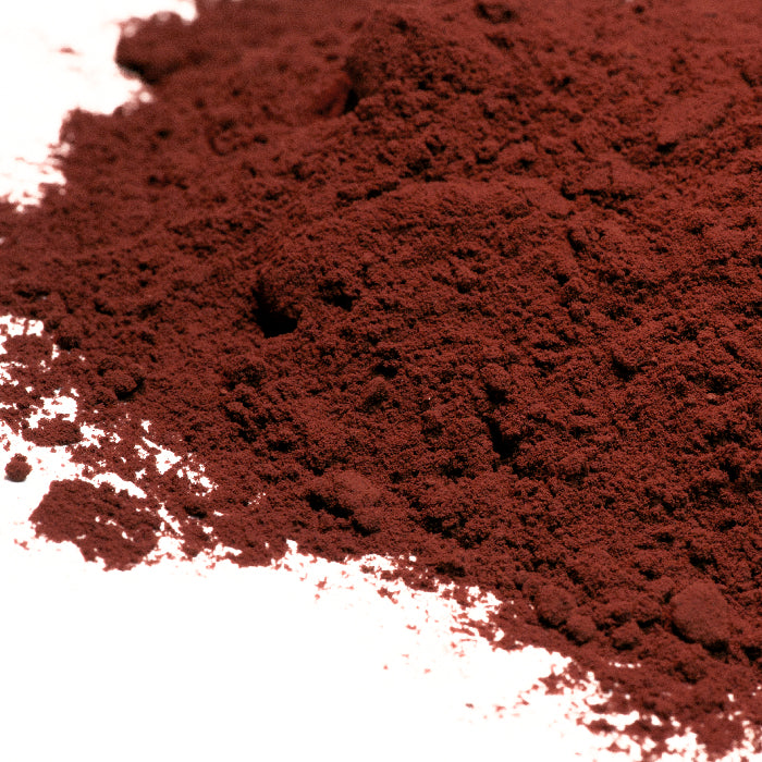 A close-up of Whole Spice Inc. Cocoa Powder, a rich reddish-brown powder, spread unevenly across a white surface.