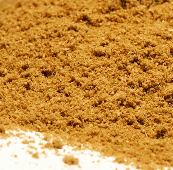 A close-up of Whole Spice Inc. Coriander Powder—light brown and finely ground—spreads across a white surface, perfect for Thai curries or pickling spice blends.