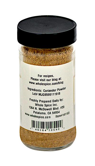 A clear spice jar with a black lid, labeled on the back as Coriander Powder. The label lists uses like Thai curries or pickling and gives Whole Spice Inc.’s address plus website for recipes.