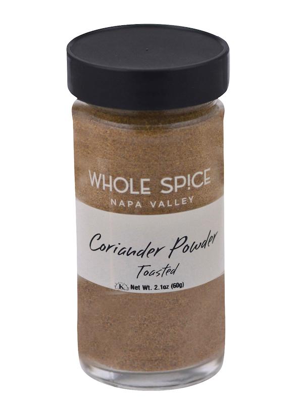 A clear glass jar with a black lid contains Coriander Powder Toasted by Whole Spice Inc., Net Wt. 2.1oz (60g), made from premium toasted coriander seed.