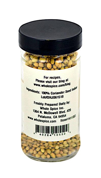 A clear glass jar with a black lid contains Whole Spice Inc. Coriander Seed Whole Indian—100% coriander seed. The label includes company info and website for recipes to add tangy flavor to authentic Indian dishes.