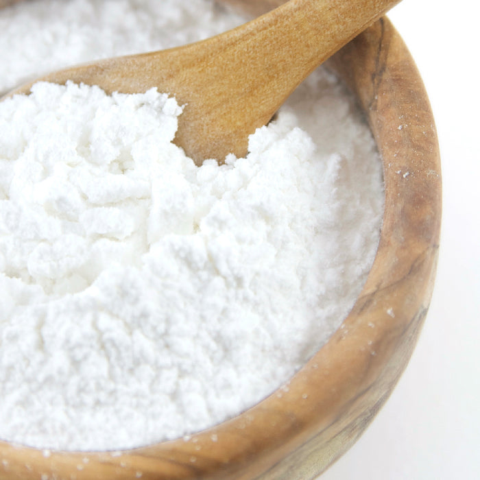 A wooden spoon rests in a wooden bowl filled with Whole Spice Inc. Cream of Tartar, a fine white powder often used to stabilize egg whites in baking.
