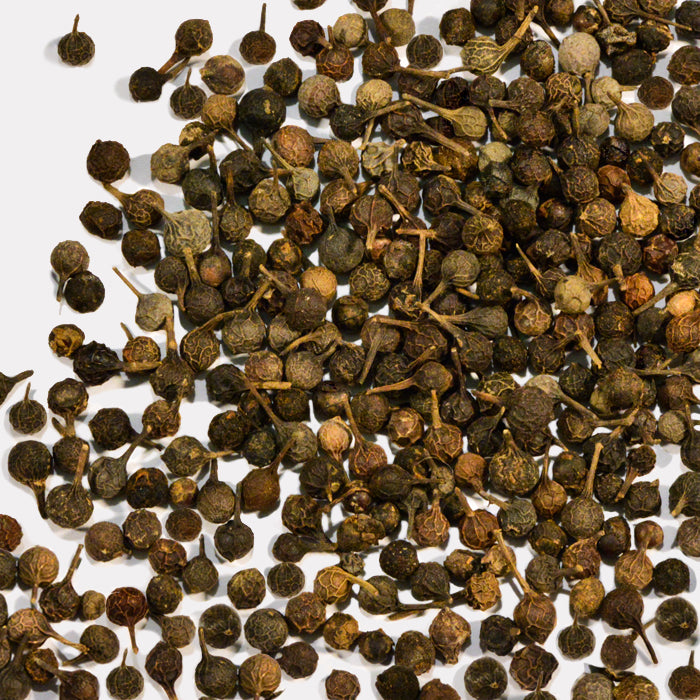 Whole Spice Inc. Cubeb Berries, with their dried, round shape and distinctive tails, are scattered on a plain white background.