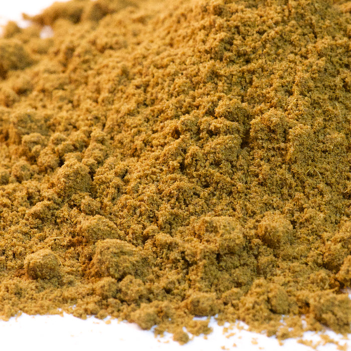 A close-up view of a textured, crumbly pile of greenish-brown Cumin Powder from Whole Spice Inc., resembling garam masala or other culinary seasonings.