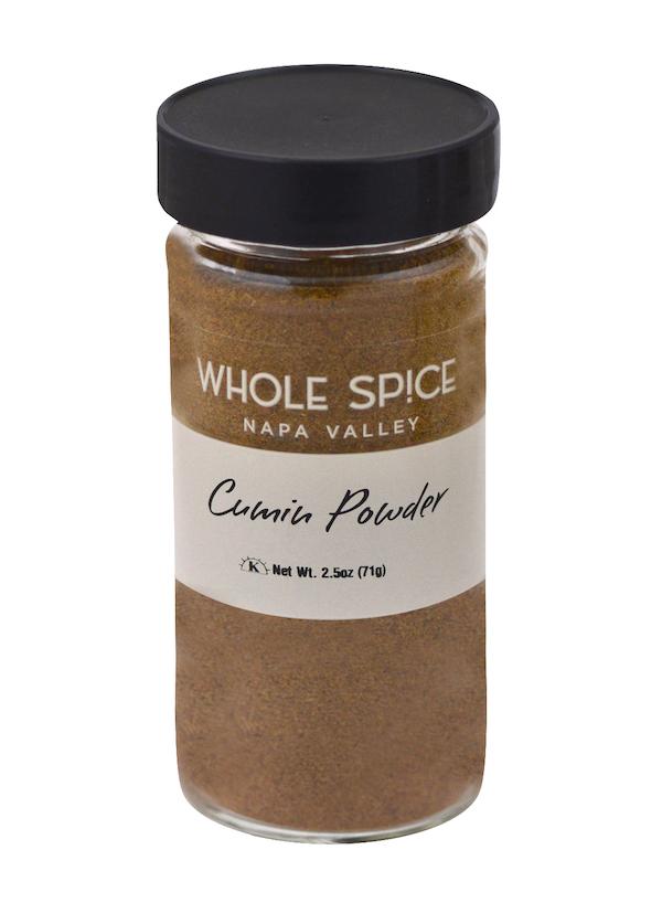 A glass jar with a black lid labeled “Whole Spice Inc. Cumin Powder”—net weight 2.5 oz (71 g)—contains light brown ground cumin, commonly used in garam masala blends.
