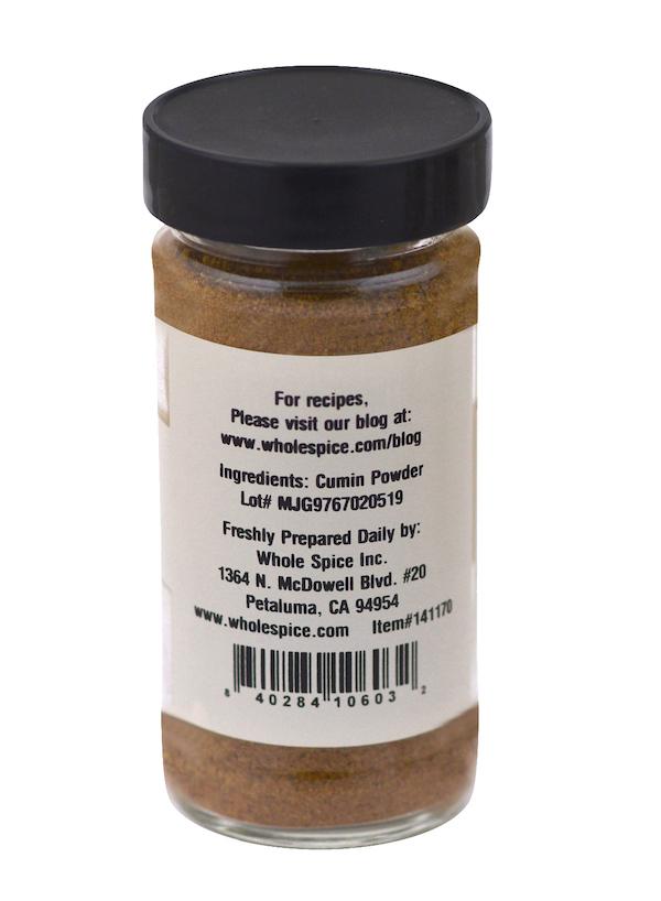 A clear spice jar with a black lid from Whole Spice Inc., labeled "Cumin Powder" with company contact info and barcode—ideal for recipes featuring garam masala.
