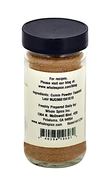 A clear spice jar with a black lid features a back white label listing Cumin Powder Toasted as the ingredient, along with Whole Spice Inc.’s contact information and website.