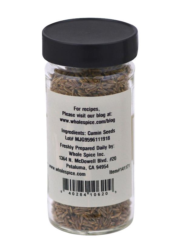 A clear glass jar with a black lid holds Cumin Seeds from Whole Spice Inc. The label lists cumin seeds as the ingredient and includes the manufacturer’s address, website, and a barcode.