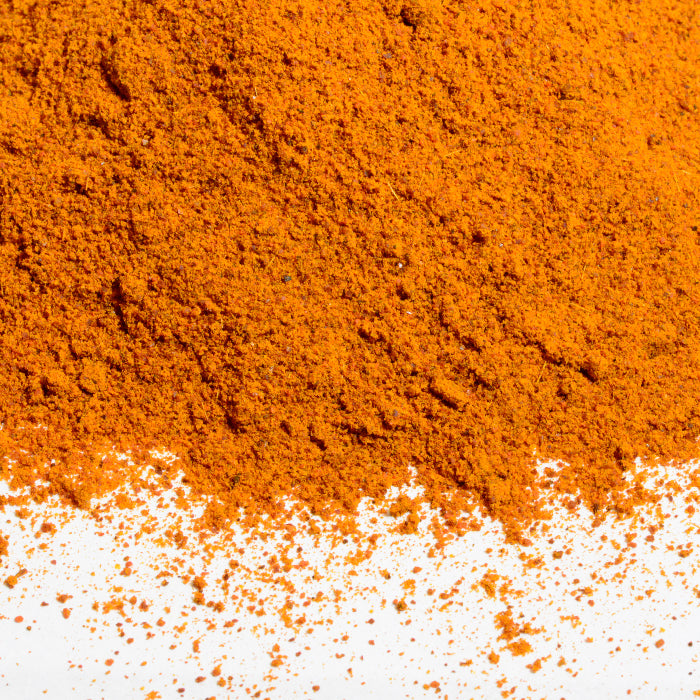 A close-up of vibrant Basic Curry Powder Organic by Whole Spice Inc., a staple in Indian cuisine, scattered on a white surface with some of the organic spice loosely spread at the edges.