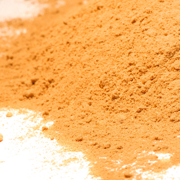 A close-up of Whole Spice Inc. Galangal Powder shows its fine orange-brown grains on a white surface—ideal for adding authentic flavor to Thai Coconut Soup.