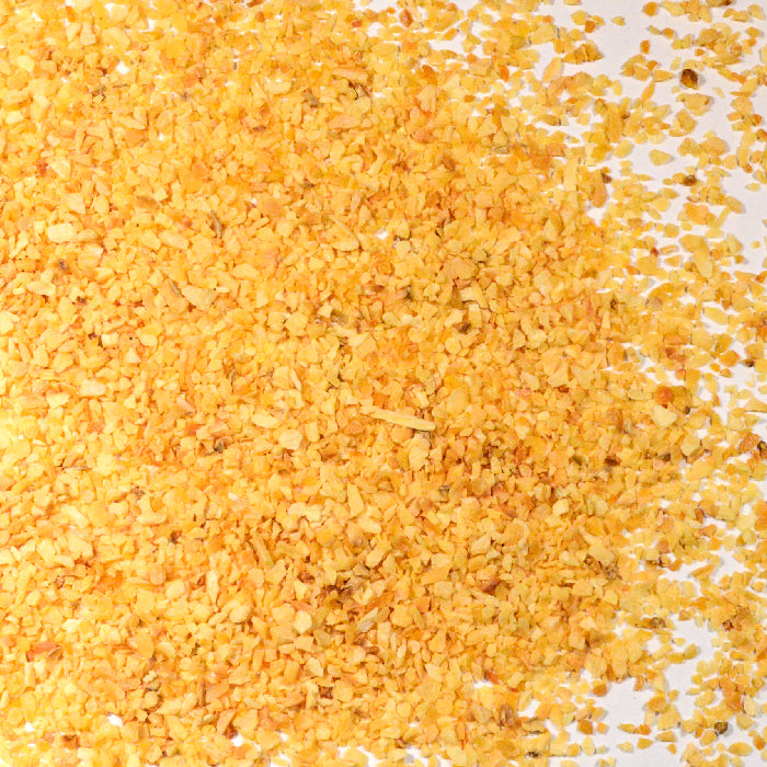 A close-up of Whole Spice Inc. Garlic Minced, showing yellow cornmeal granules mixed with dehydrated garlic spread unevenly on a white surface.