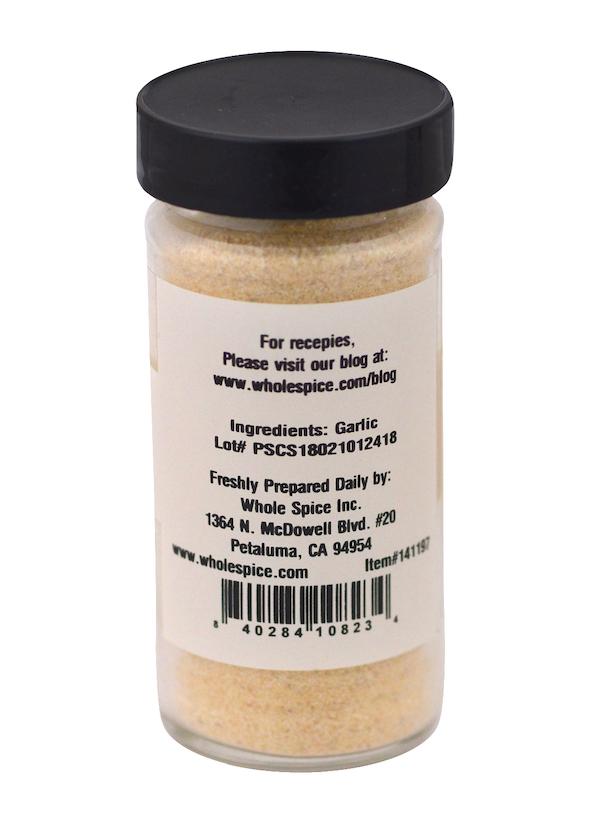 A clear spice jar with a black lid contains light Garlic Granulated powder from Whole Spice Inc. The label lists the ingredient as garlic, plus a barcode, contact info, and a website for recipes.