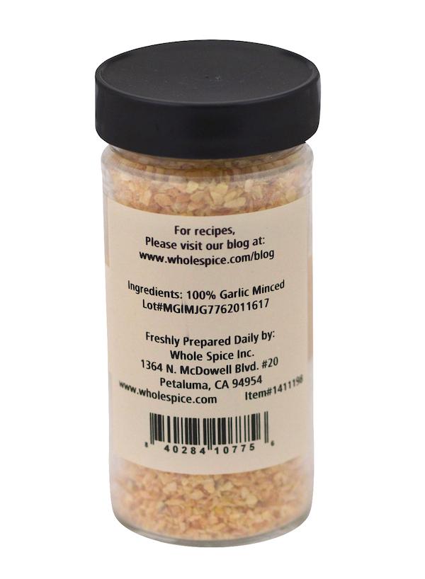 A clear plastic jar with a black lid contains Garlic Minced by Whole Spice Inc. The label lists only 100% dehydrated garlic as the ingredient, along with company contact info and a barcode.