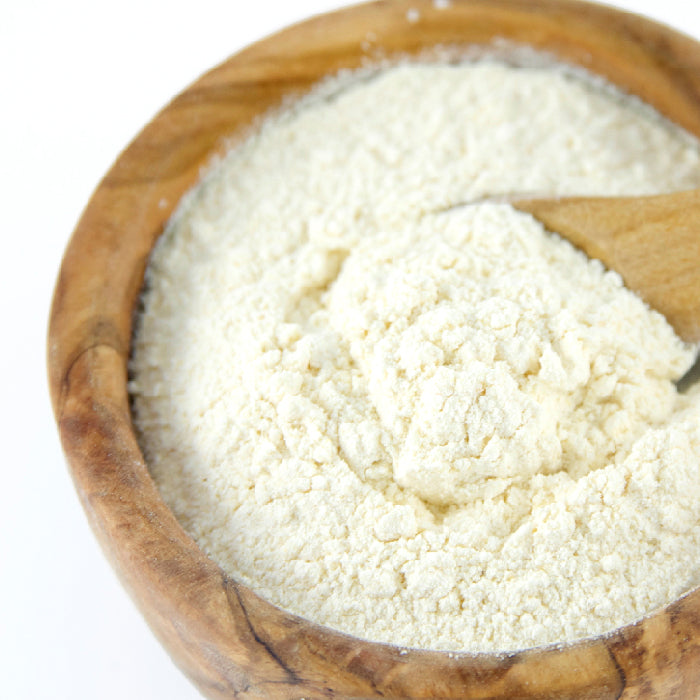 A wooden bowl of off-white Garlic Powder Organic by Whole Spice Inc., mixed with flour and a wooden spoon inside, set against a white background.