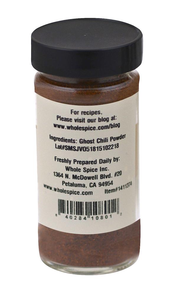 A clear spice jar from Whole Spice Inc. holds Ghost Chili Powder—fine red-brown Bhut Jolokia, the world’s hottest pepper—with a black lid and label listing ingredients, brand name, website, and company address.