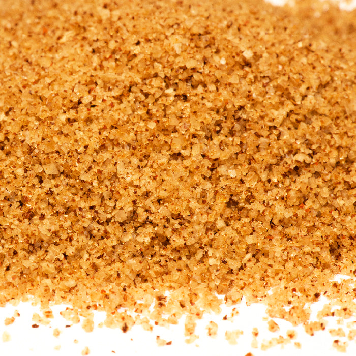 Close-up image of Ghost Salt by Whole Spice Inc.—a coarse, light brown spicy seasoning with visible granules and colorful flecks on a white background.